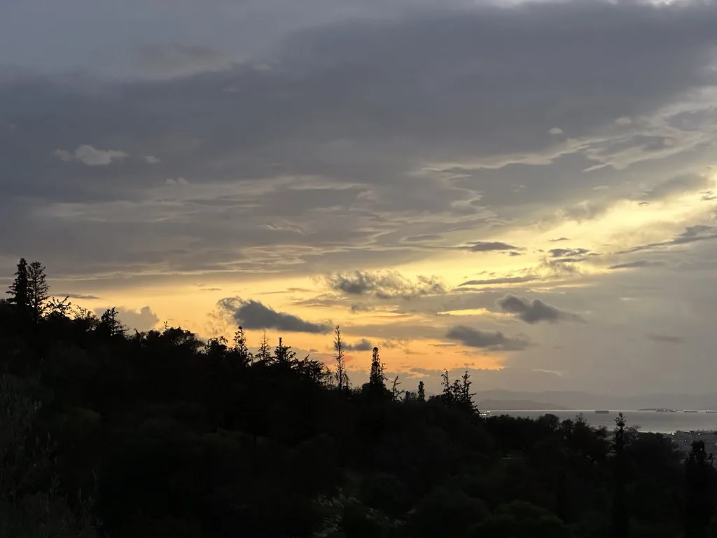 Sunset glow beneath dramatic clouds over forest near Athens, Attica, Greece, November
